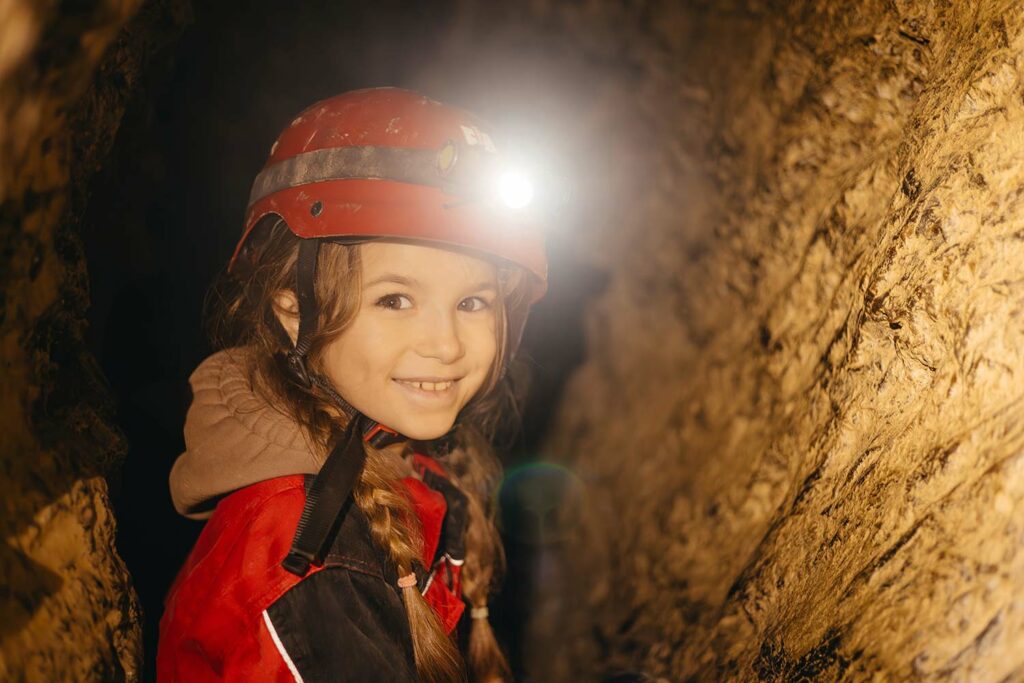 Mädchen mit Stirnlampe hofft in der Einhornhöhle darauf, die scheuen Fabelwesen zu entdecken.