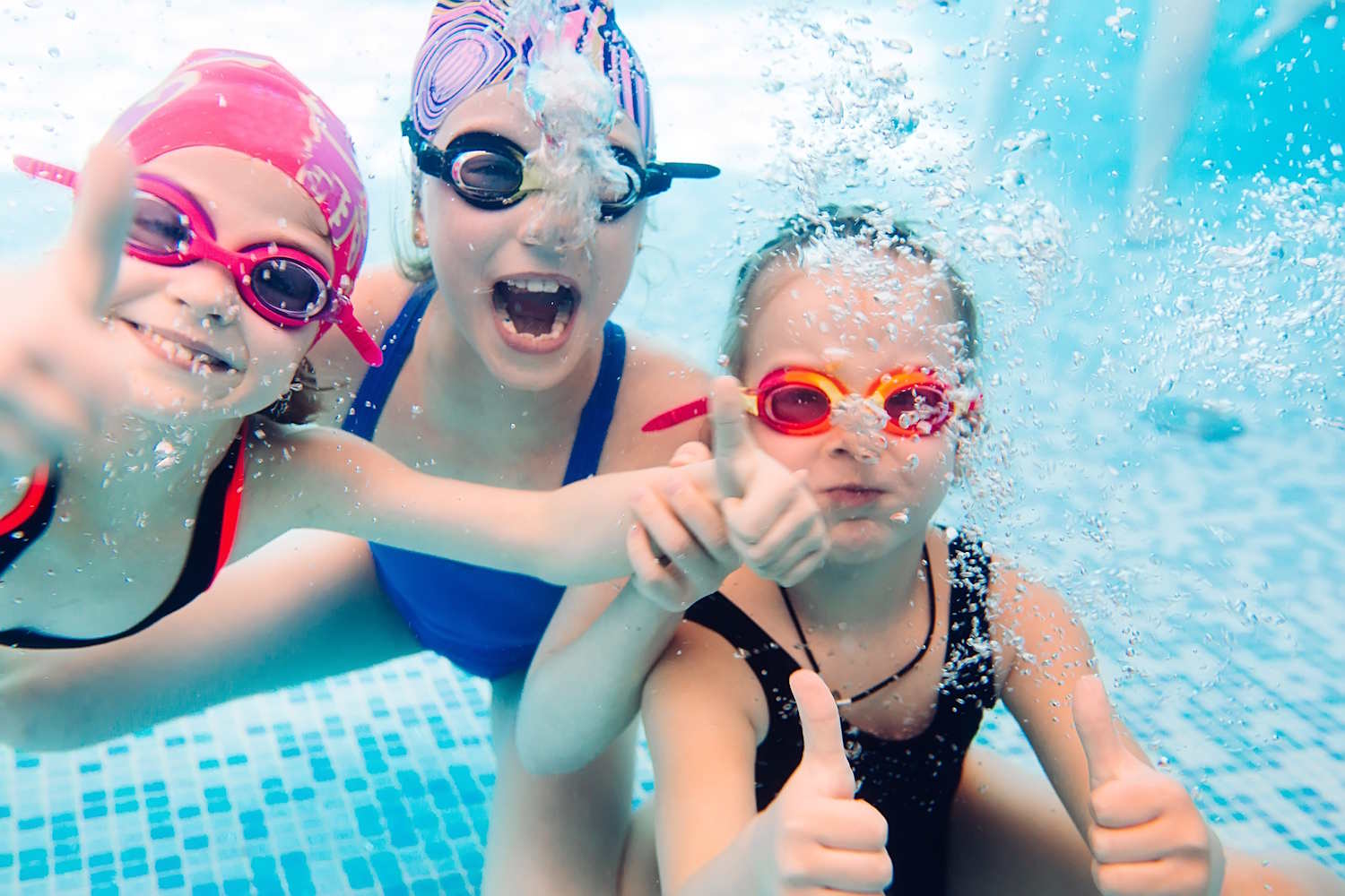 Unterwasserbild von 3 lachenden Kindern mit Schwimmbrillen im Schwimmbad